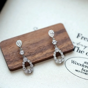 Elegant silver teardrop earrings with white zircon crystals on a dark wood display