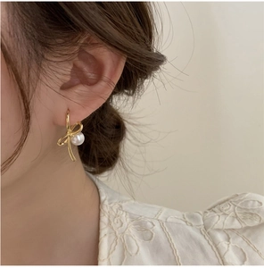 Détail de boucles d'oreilles nœud élégantes avec lignes dorées et perle sur un mannequin
