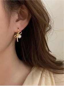 Détail de boucles d'oreilles nœud dorées avec perles blanches portées par un modèle