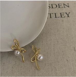 Détail de boucles d'oreilles nœud doré avec perles blanches sur tissu texturé