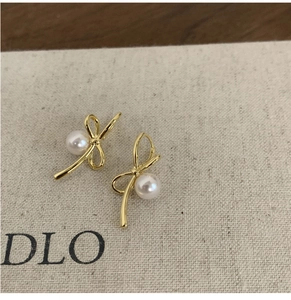Gros plan de boucles d'oreilles nœud doré avec perles blanches sur toile beige