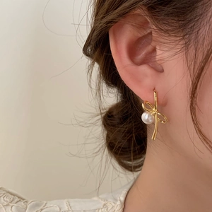 Élégantes boucles d'oreilles nœud doré avec perle sur mannequin pour un look chic