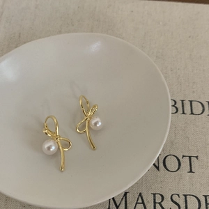 Boucles d'oreilles nœud dorées avec perles sur une assiette en céramique blanche