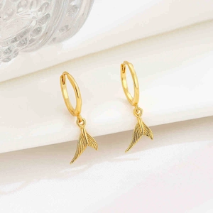 Detail of gold fishtail drop earrings on white silk fabric with soft lighting effects