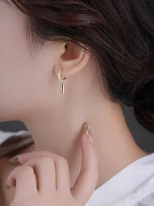 Detailed close-up of C-shaped earrings with gold cylinder drops and shimmering white pavé stones