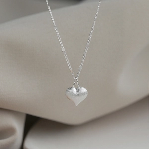 Macro detail of silver heart pendant with a matte frosted finish and elegant thin chain