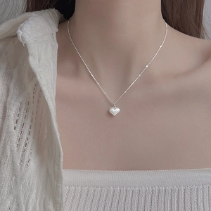 Close-up of matte heart pendant necklace on model wearing a white knit sweater