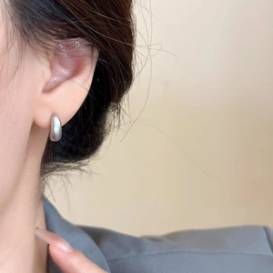 Close-up of minimalist silver C-shaped teardrop stud earrings with a brushed matte finish