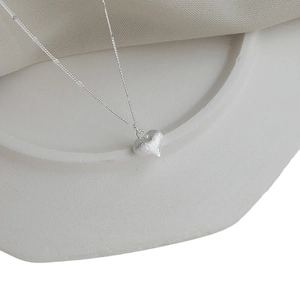 Elegant silver heart pendant necklace with matte finish on white stone display stand