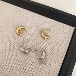 Macro detail of C-shaped matte metal stud earrings in gold and silver finish