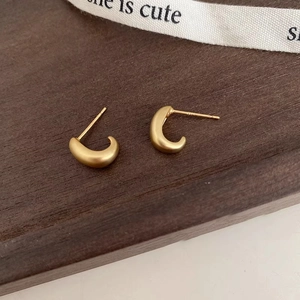 Macro shot of minimalist C-shape matte gold earrings with s925 silver studs on wood