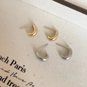 Macro shot of minimalist C-shape drop earrings in matte gold and silver brushed metal