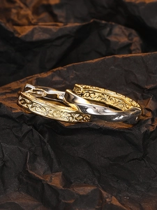 Macro detail of textured gold relief and silver twisted hoops on black paper