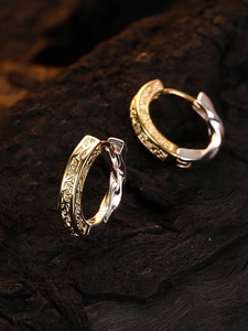 Macro shot of textured gold and silver mixed-metal hoop earrings on a dark wood base