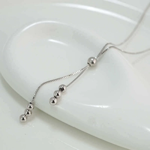 Minimalist silver bead tassel necklace with high polish finish on a smooth white surface