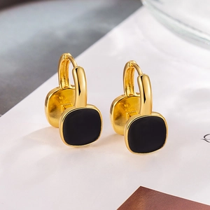 Macro shot of minimalist gold square hoop earrings with black inlay on white background