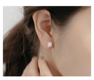 Close-up of a silver hollow four-leaf clover stud earring worn on a model's ear