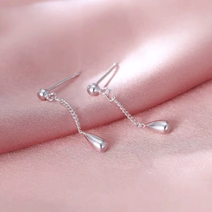 Macro shot of silver teardrop tassel earrings on soft pink satin fabric background