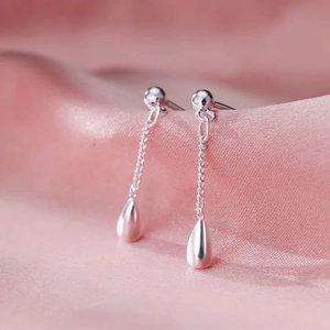 Macro view of silver teardrop tassel earrings on elegant pink silk fabric background