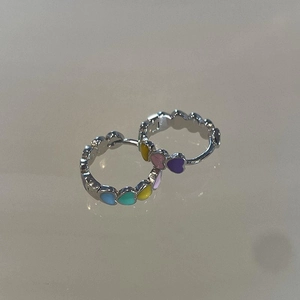 Détail des créoles argentées avec breloques en émail en forme de cœurs multicolores