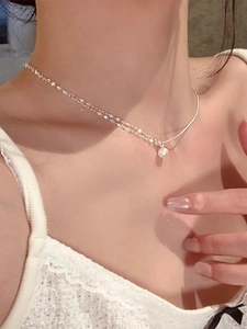Detail of silver layered chain necklace with a single pearl pendant on a model's neck