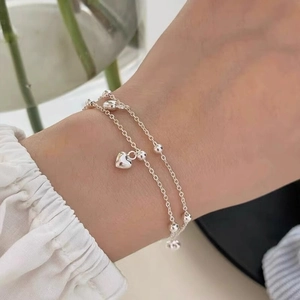 Elegant double-layered silver heart pendant bracelet with beads on woman's wrist