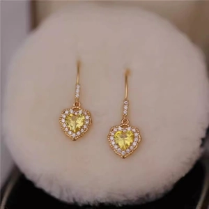 Close-up of gold drop earrings featuring yellow heart-shaped crystals and sparkling pavé