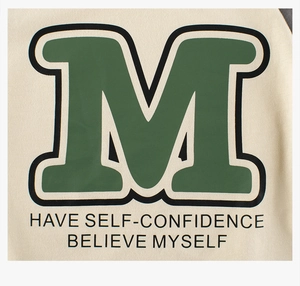 Detail of boys raglan tee showing green M letter print and inspirational typography