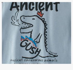Gros plan de l'imprimé dinosaure rétro avec couronne rouge sur ce t-shirt en coton bleu