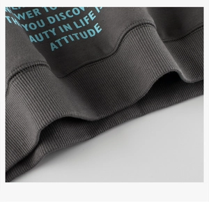 Macro detail of dark grey sweatshirt featuring blue attitude text and ribbed hem texture