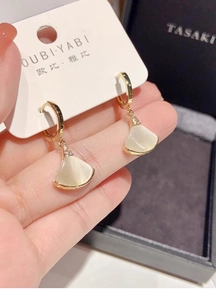 Detalle de pendientes dorados en forma de abanico con nácar blanco y pequeños diamantes