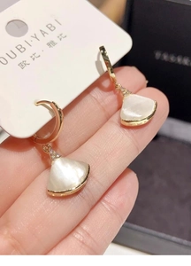 Detalle de pendientes dorados en forma de abanico con nácar y pequeños cristales finos