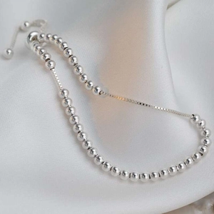 Dettaglio di un braccialetto a sfere d'argento regolabile con chiusura a scorrimento su seta
