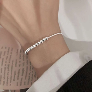 Primo piano di un bracciale minimalista con perline d'argento indossato su uno sfondo grigio
