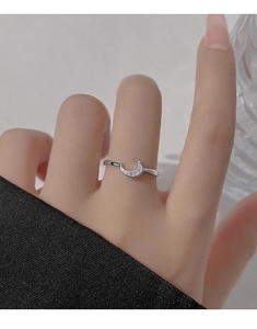 Close-up of a minimalist silver crescent moon ring with sparkling zircon stones on a hand