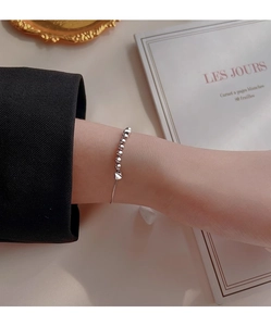 Gros plan d'un bracelet à perles argentées avec cœur au poignet et manche noire chic