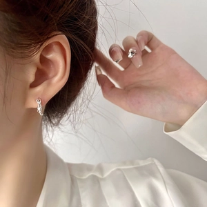 Close-up of minimalist twisted silver hoop earring worn by a model in soft lighting