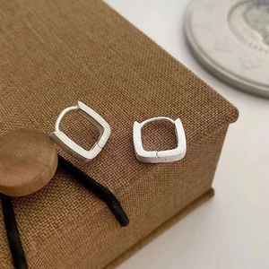 Macro view of minimalist square silver hoop earrings with a brushed metal texture
