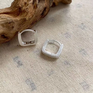 Close-up of minimalist square silver earrings with a brushed matte texture on linen background