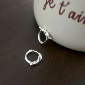 Close-up of silver knot earrings with shiny finish on a vintage wooden tabletop background