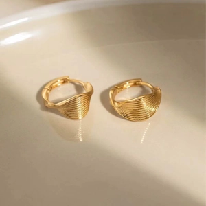 Macro shot of gold-plated hoop earrings with wavy texture on a white ceramic tray