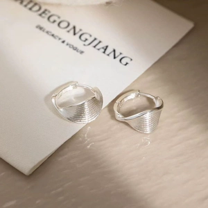 Detail of twisted silver earrings with fine textured ridges and glossy metallic finish