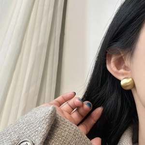 Close-up of minimalist golden round stud earrings worn by a model with a grey coat