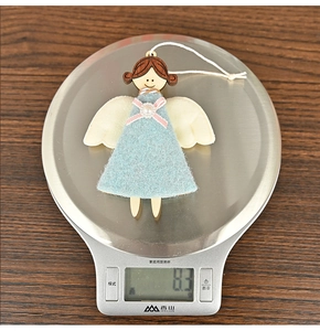 Détail d'un petit ange en bois et feutrine bleue pesant 8,3 g sur une balance