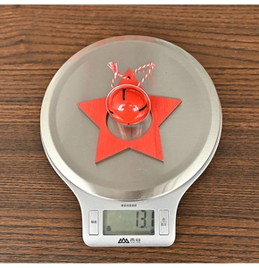 Detailed view of red wooden star ornament with metal bell being weighed on a scale