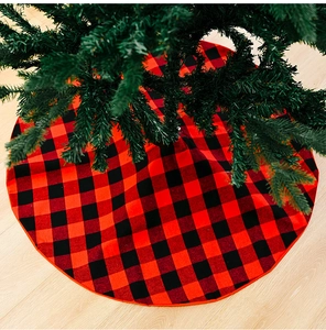 Detail of red and black buffalo plaid Christmas tree skirt on wooden floor with green branches