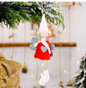 Detail of plush Christmas angel ornament with red fur and silver heart on a pine branch