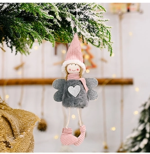 Detail of plush angel ornament with pink knit hat and silver glitter heart on a snowy tree