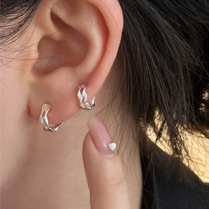 Silver wavy hoop earrings in fluid metal design worn on ear with polished finish
