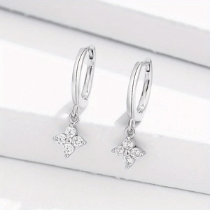 Close-up of silver four-leaf clover earrings with cubic zirconia stones on white steps